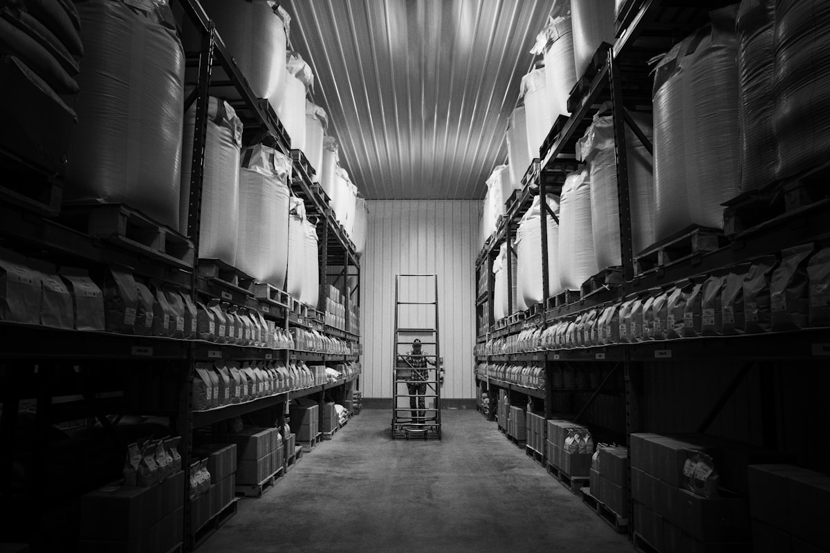 A picker on a ladder working a narrow aisle of labelled shelves